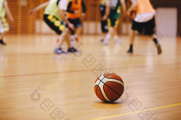 篮球训练比赛背景。篮球在木制的球场地板上特写，模糊的球员在背景中打篮球