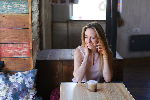 年轻的女人坐着舒适的咖啡房子表格玻璃杯卡布奇诺咖啡聊天智能手机