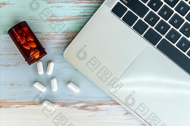 顶视图药丸药瓶中溢出的药物，复古木制背景上有笔记本电脑