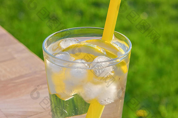 桌上放一杯简单的冰水，柠檬片和吸管。在户外拍摄，背景为不对焦的草地，采用柔软的su