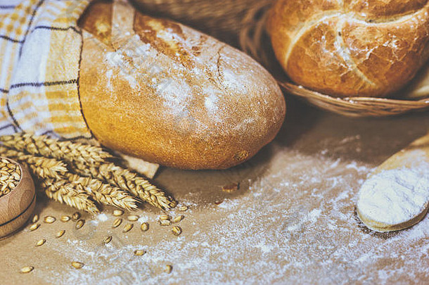 两种不同类型的新鲜烘焙面包的特写镜头，背景为质朴的小麦和面粉。面包店和杂货店的概念。复古麦田照片