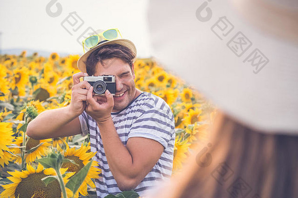 年轻的赶时髦的人的家伙采取照片女朋友复古的古董相机向日葵场爱旅行夏天概念