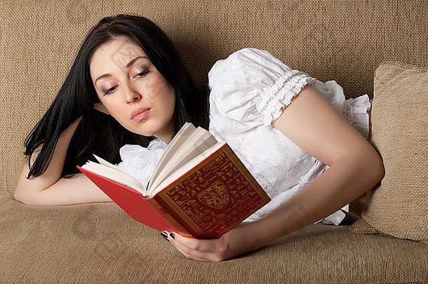 美丽的女人在沙发上读她最喜欢的书