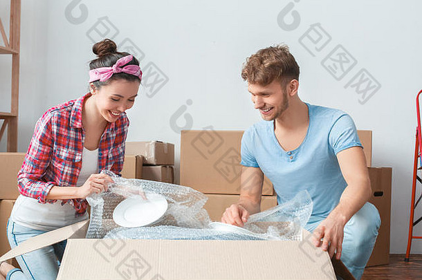 这对年轻夫妇搬到新的地方，坐在盒子旁边，开心地打开盘子