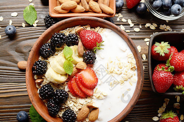 在木制厨房桌子上的粘土盘中，可以俯瞰水果健康的<strong>慕斯</strong>丽，香蕉、草莓、杏仁、黑莓和酸奶