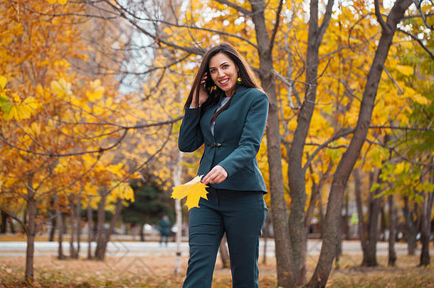 打电话的女人。穿着蓝色套装的快乐成功的阿拉伯女商人在秋天公园散步