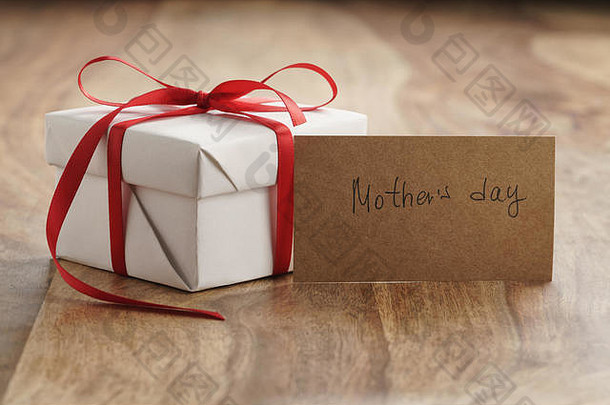 旧木桌上的白色礼品盒，带有红色细丝带和母亲节卡片