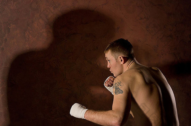 在一场拳击比赛中，这位年轻坚定的拳击手蜷缩着身体向前，举起包扎好的拳头，侧视图留有空间