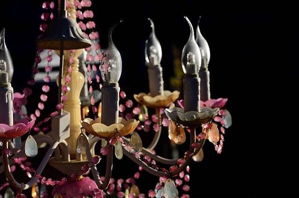 一盏由粉色塑料和人造蜡烛制成的俗气吊灯悬挂在黑暗的背景下