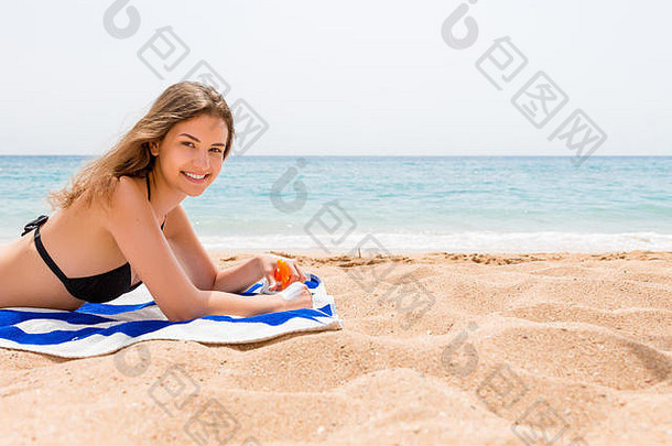 年轻快乐的女人在海边的毛巾上休息，用防晒霜保护手上的皮肤不受喷雾的伤害。