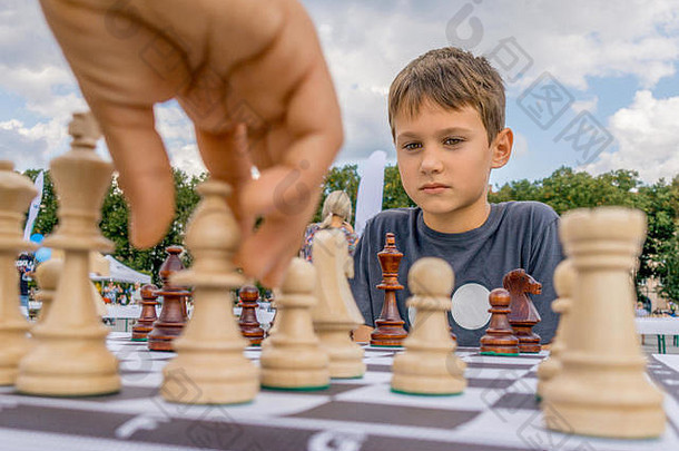 孩子们在户外的棋盘上下棋。一个认真思考国际象棋组合的男孩