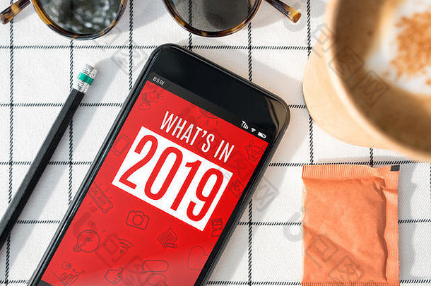 2019年手机的俯视图，咖啡杯，太阳镜，白色桌布上的铅笔。数字影响者博客生活方式。
