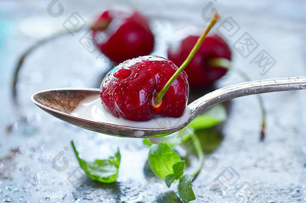 在一个勺子上用奶油和黑樱桃做特写，更多的樱桃和新鲜薄荷叶放在肮脏的金属背景上