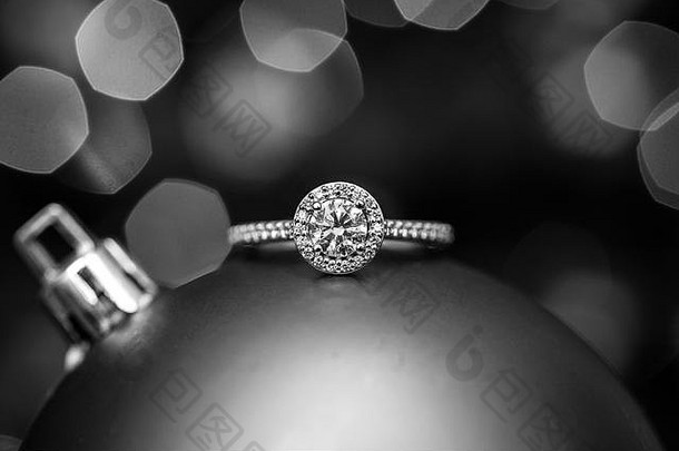 背景为灯光的圣诞装饰品上的订婚戒指。非黑即白的