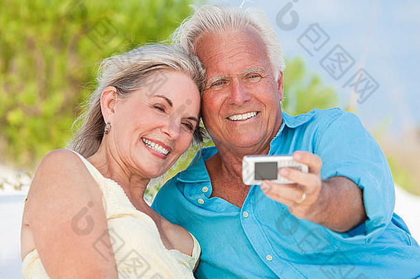 一对快乐的老年男女在热带海滩上用手机笑着拍照