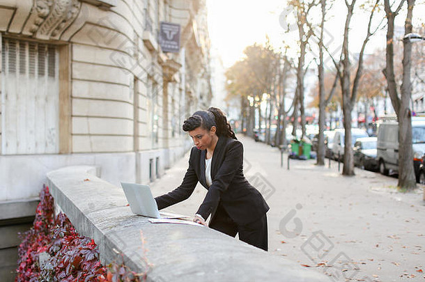一半的非洲女商人在阳台上用笔记本电脑工作。