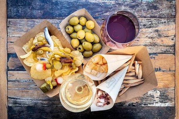 塔帕斯和平丘斯，从上方拍摄。木桌上放着奶酪、果酱和橄榄、吉尔达斯和薯片，还有一杯红酒和白酒