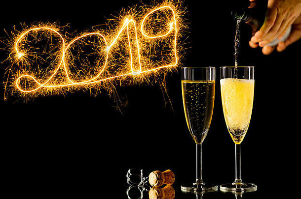新年快乐两杯香槟和美丽闪亮的金色数字2019，在纽约的黑色背景上用火花焰火书写
