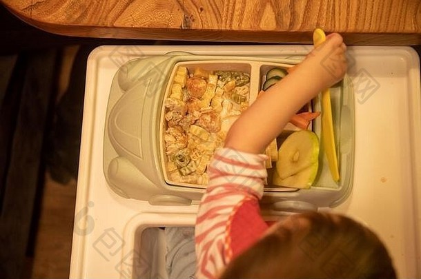 俯视图，孩子坐在一个装满美味令人垂涎欲滴食物的儿童盘子前，拿着一把儿童塑料刀。软焦点。