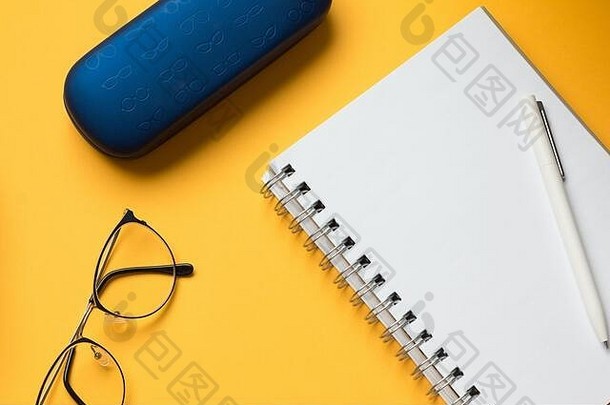 一张空白打开的笔记本页面、眼镜和黄色背景上的蓝色盒子的库存照片