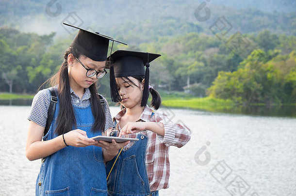 两个小女孩在大自然中使用平板电脑，具有复古的色调，教育理念。