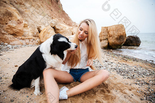 微笑迷人的年轻的女人坐着玩狗海滩