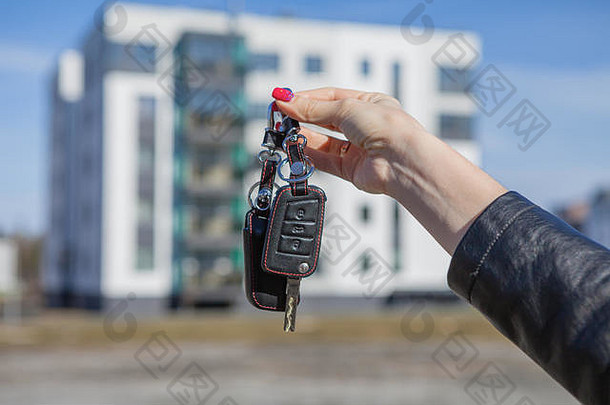 在一座新房子模糊的背景上，一个女孩手里拿着汽车钥匙