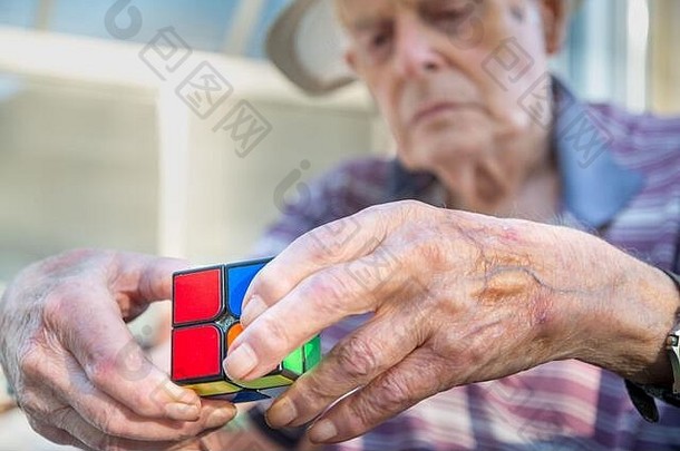 特写镜头：一位老人使用Rubix立方体拼图作为治疗手段，治疗他因头部受伤和脑损伤而导致的智力下降
