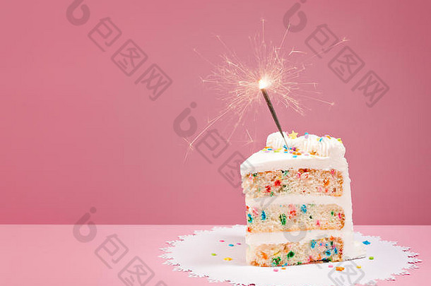 一块彩色生日彩纸蛋糕，粉红色背景上有亮闪闪的火花。