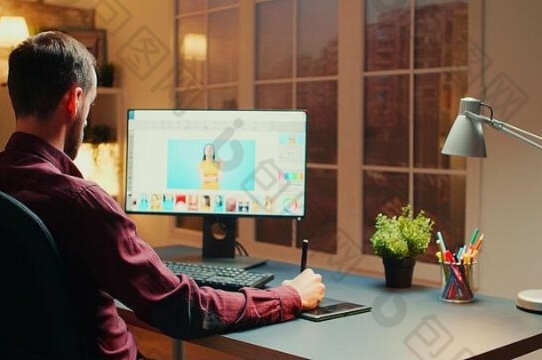 专业摄影师坐在办公桌旁，在夜间使用图形平板电脑对照片进行润色。