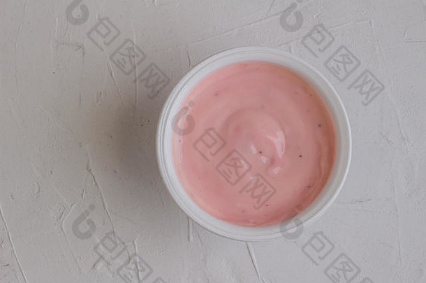 在白色乡村背景上隔离的塑料杯中，含有天然色素的健康草莓水果味酸奶-摄影棚顶视图拍摄