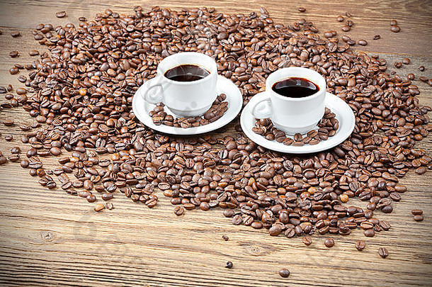 木桌上的咖啡豆中放着两个咖啡杯。