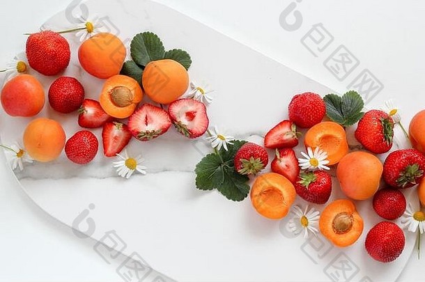白色背景上的大理石托盘上摆放着五颜六色的水果——草莓和桃子