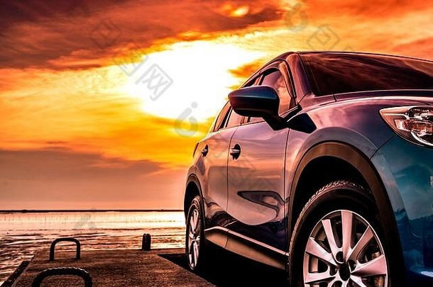 蓝色豪华SUV停在海边的水泥路上，夕阳下的天空是美丽的红色。热带海滩的暑假。公路旅行。前视运动