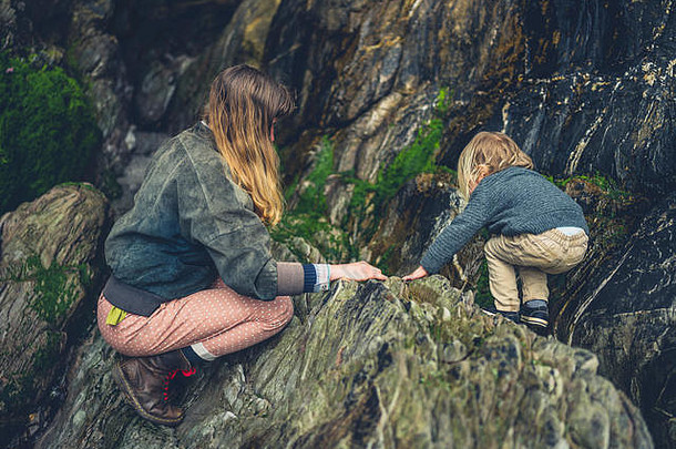 一位年轻的母亲和她蹒跚学步的孩子正在探索海滩上的岩石