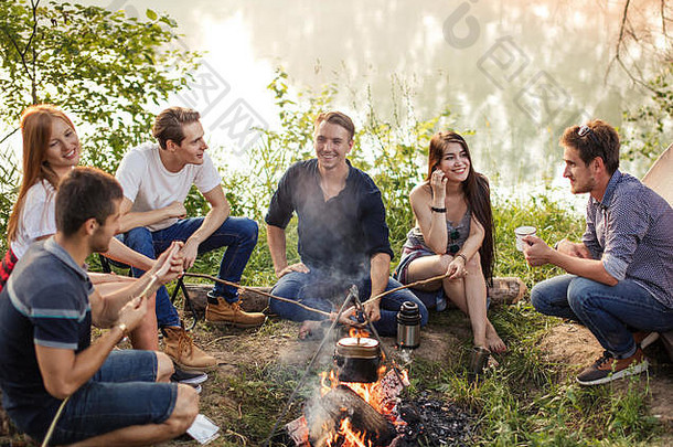 一群朋友围坐在篝火旁准备香肠。