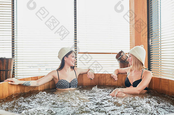 两个放松的女孩在豪华水疗中心休息一天，一边洗漩涡泡泡浴，一边分享想法和新闻