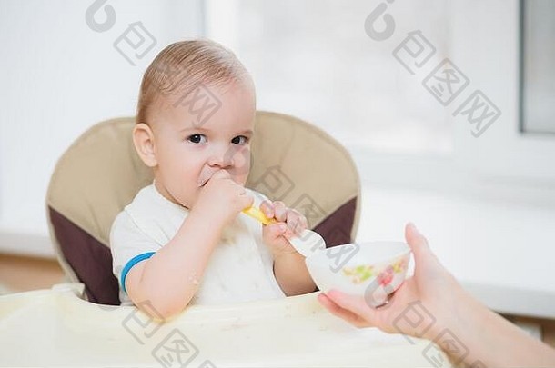 小孩坐在椅子上用勺子吃饭