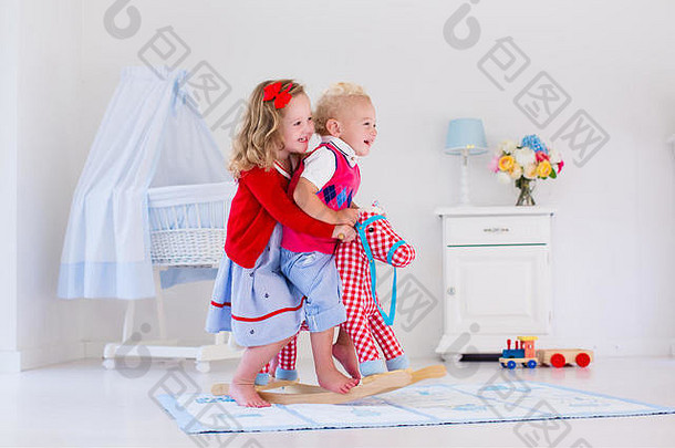 两个孩子在室内玩耍。孩子们骑着玩具摇马。在托儿所或幼儿园玩耍的男孩和女孩。