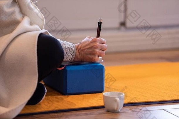 一个人在瑜伽课上以某种瑜伽姿势在笔记本上做笔记。学习瑜伽的学徒