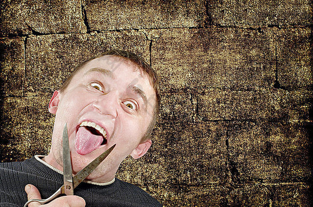 拿着剪刀的疯子在肮脏的砖墙背景上割断了自己的舌头。