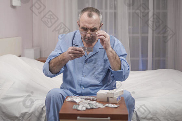 生病的老人坐在床上，选择药物和药片。
