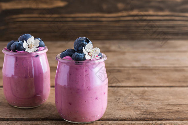 两杯蓝莓酸奶，配上新鲜蓝莓和春花，以乡村木质为背景，打造健康早餐。闭合