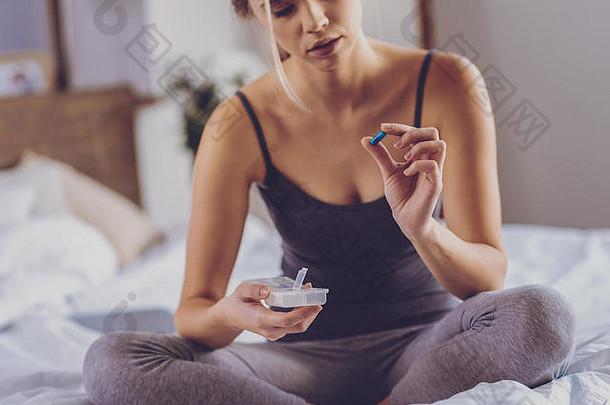 愉快的年轻的女人检查蓝色的止痛药胶囊