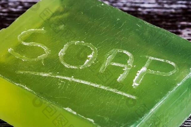 特写，一块天然肥皂的浅焦点，侧面刻有字母。这种肥皂颜色半透明，可以看到它躺在天然木材上。