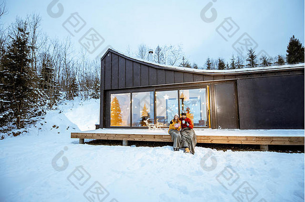 年轻的夫妇气候变暖格子热饮料坐着阳台现代房子山杜尔尼格冬天假期宽陆地视图