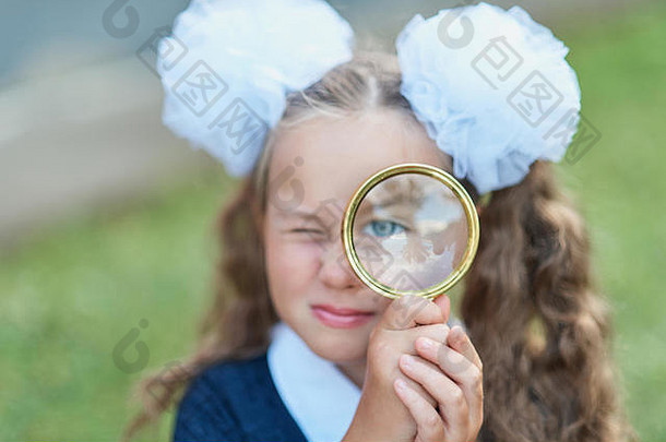 一位年轻漂亮的女学生透过放大镜端坐在背景秋园的书桌前的肖像。告别钟。年月日