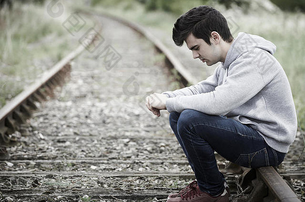 抑郁年轻的男人。坐着铁路跟踪