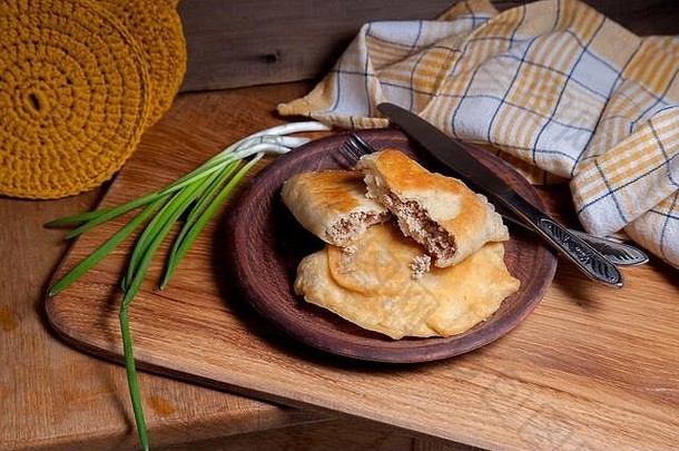 木桌上放着两个单独的带肉的油炸馅饼。快餐餐盘的成分——两个派和拉猪肉糕点，