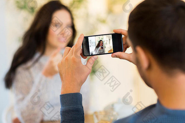 男子在咖啡馆用智能手机拍摄女子照片